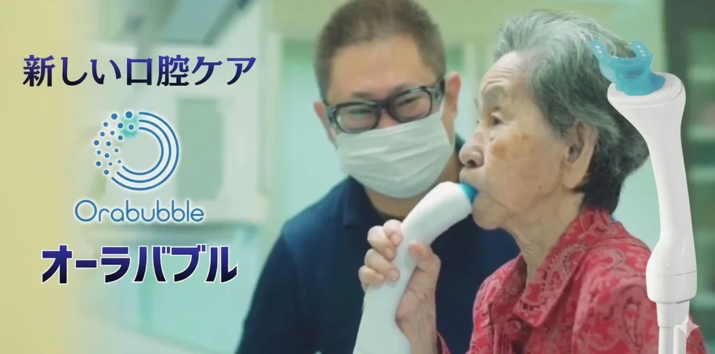 高齢者がオーラバブルを口にくわえて口腔洗浄をしている様子とそれを見守る介護者の２人の写真