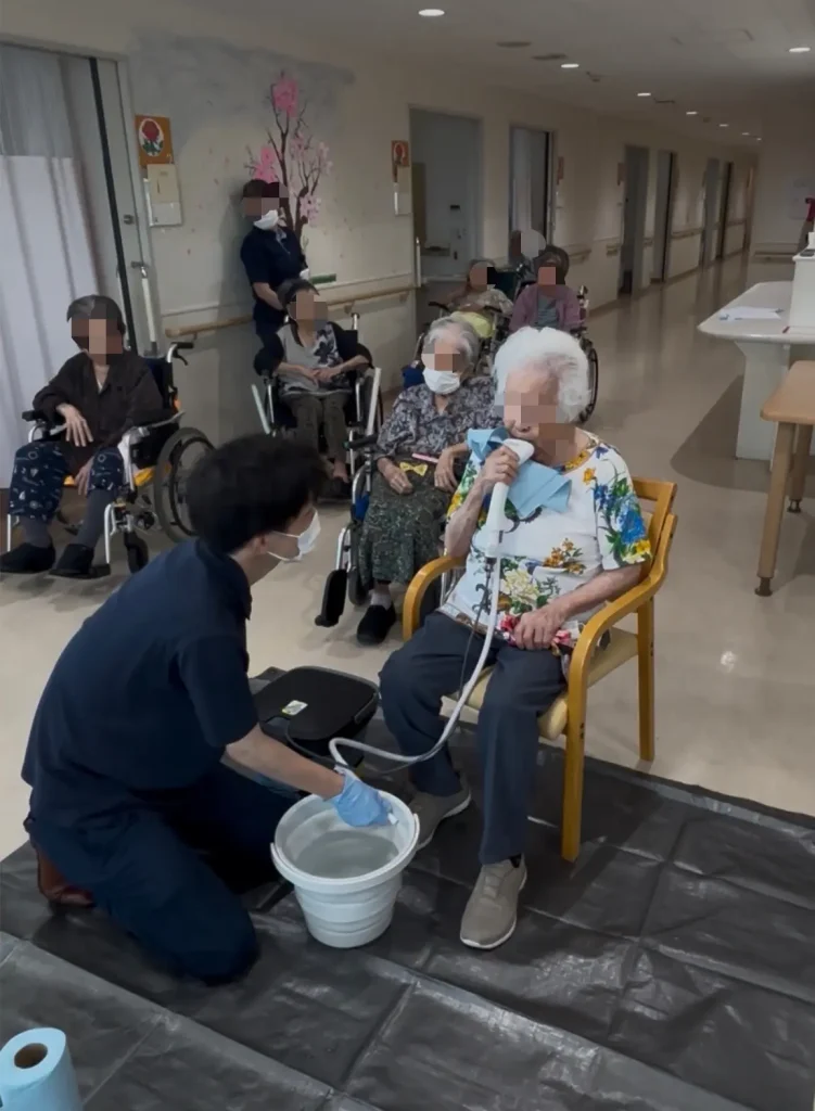 特別養護老人ホームでのオーラバブルデモンストレーション。スタッフが排水管理をしながら利用者が体験する様子